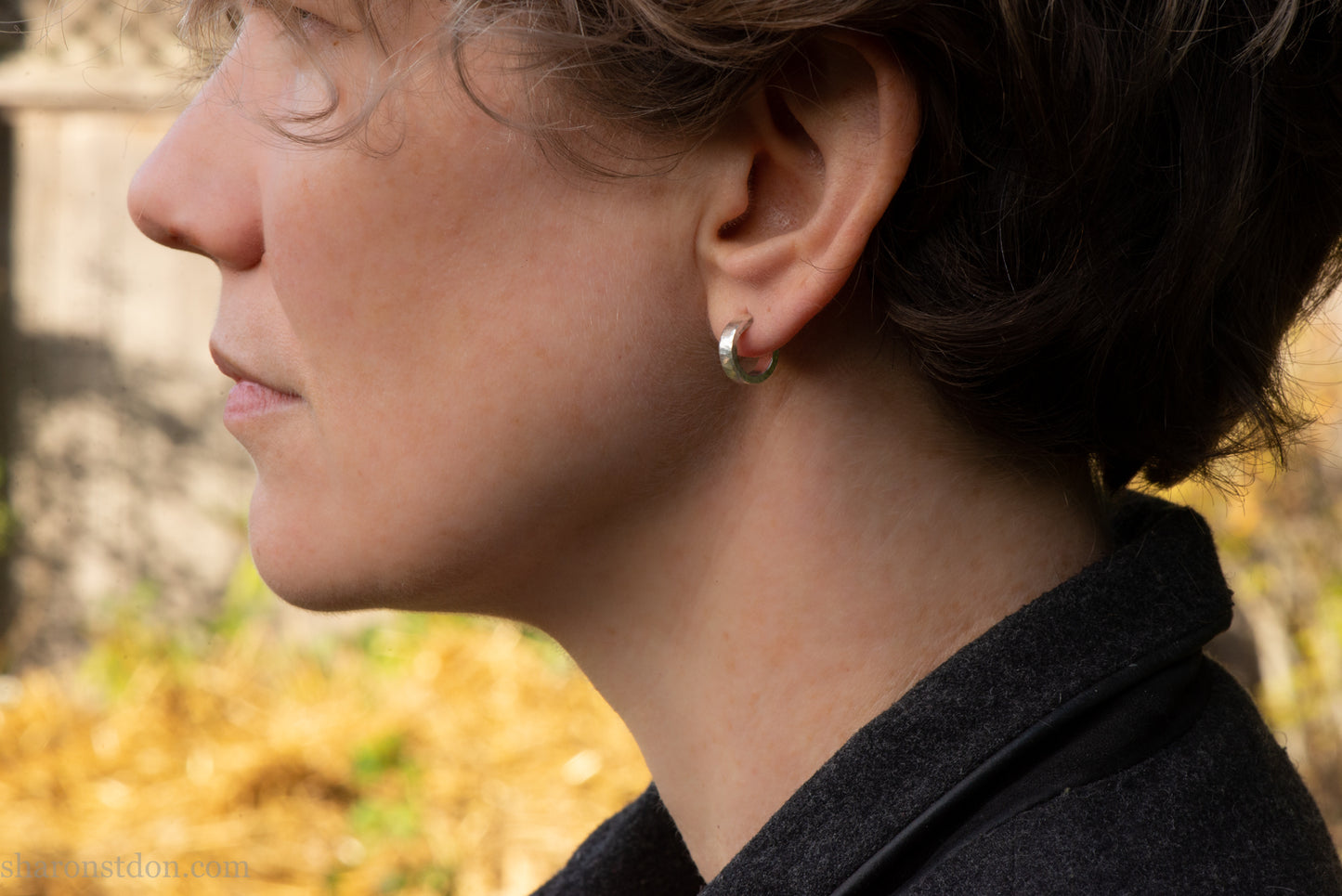 A close-up profile view of a woman's face, focusing on her earrings and the background.