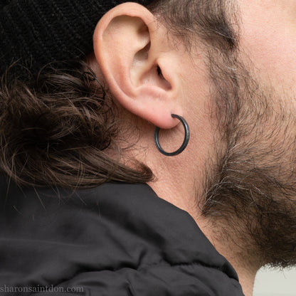 Hand hammered 925 sterling silver hoop earrings with an oxidized black finish. 20mm diameter x 2mm wide x 1.5mm thick, worn on an ear.