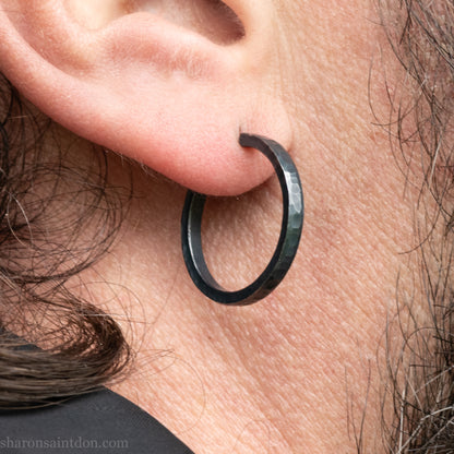 Hand hammered 925 sterling silver hoop earrings with an oxidized black finish. 20mm diameter x 2mm wide x 1.5mm thick, worn on an ear.
