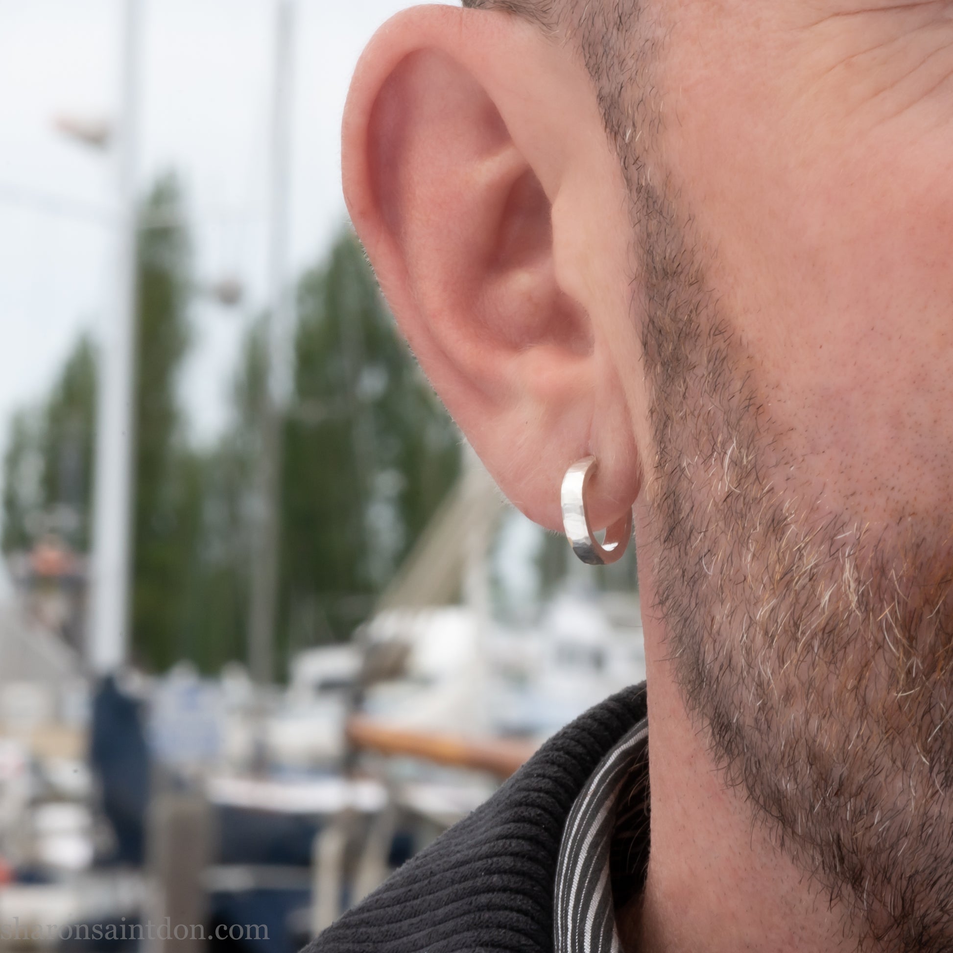 A close-up view of a man wearing handcrafted solid silver hoop earrings, 14mm diameter x 3mm wide x 1.5mm thick with a hammered matte finish.