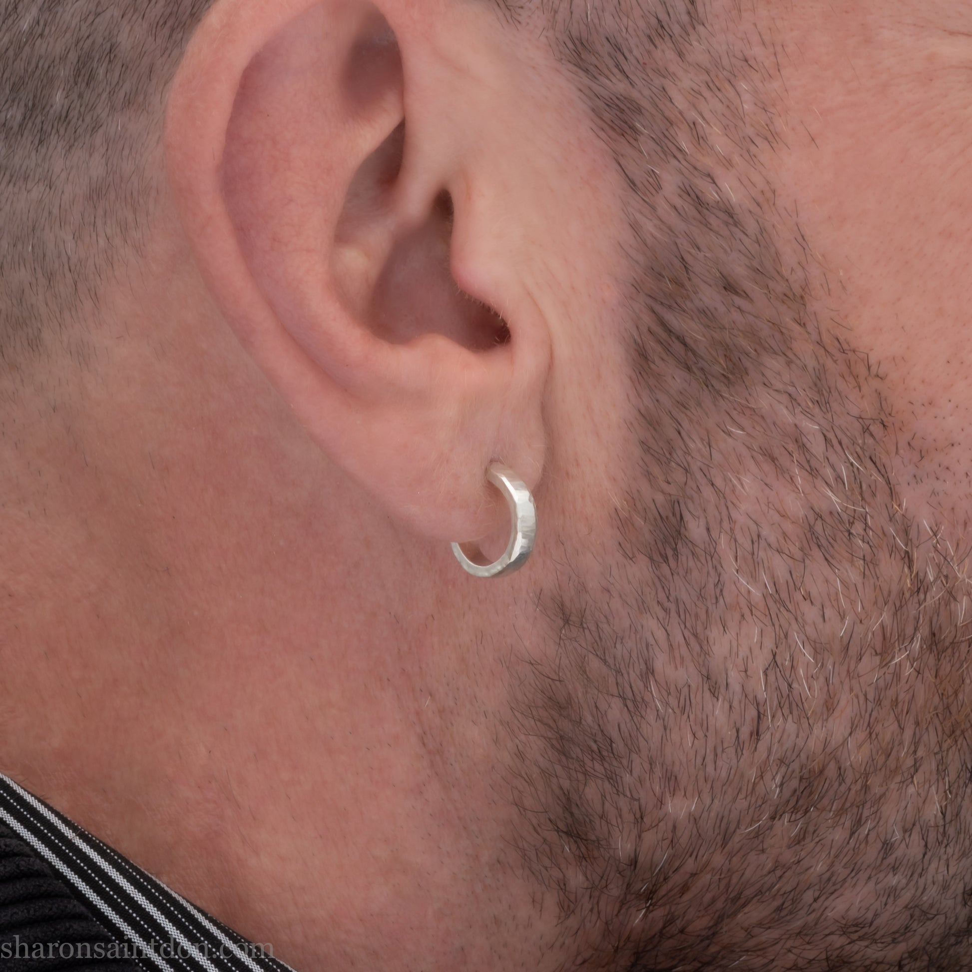 A close-up view of a man wearing handcrafted solid silver hoop earrings, 14mm diameter x 3mm wide x 1.5mm thick with a hammered matte finish.