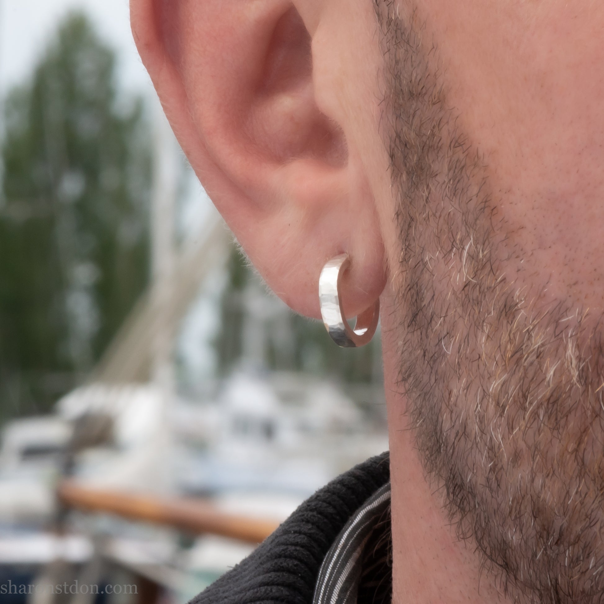 A close-up view of a man wearing handcrafted solid silver hoop earrings, 14mm diameter x 3mm wide x 1.5mm thick with a hammered matte finish.