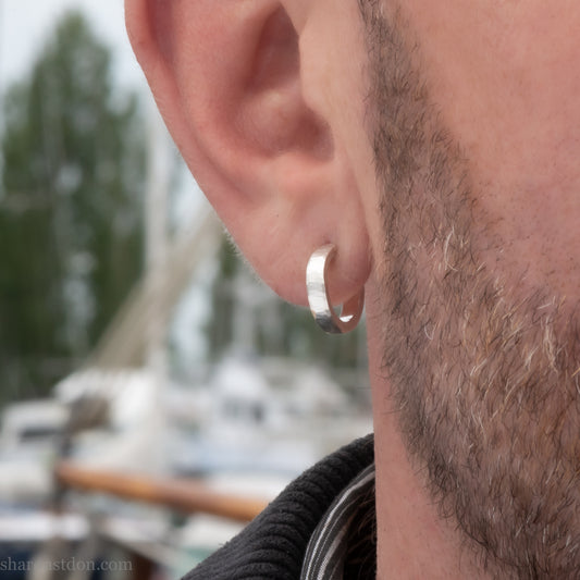 A close-up view of a man wearing a handcrafted solid silver hoop earring, 14mm diameter x 3mm wide x 1.5mm thick with a hammered matte finish.