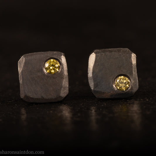 Handcrafted sterling silver square stud earrings with a 2mm canary yellow diamond set in the corner, hammered texture, oxidized black finish.