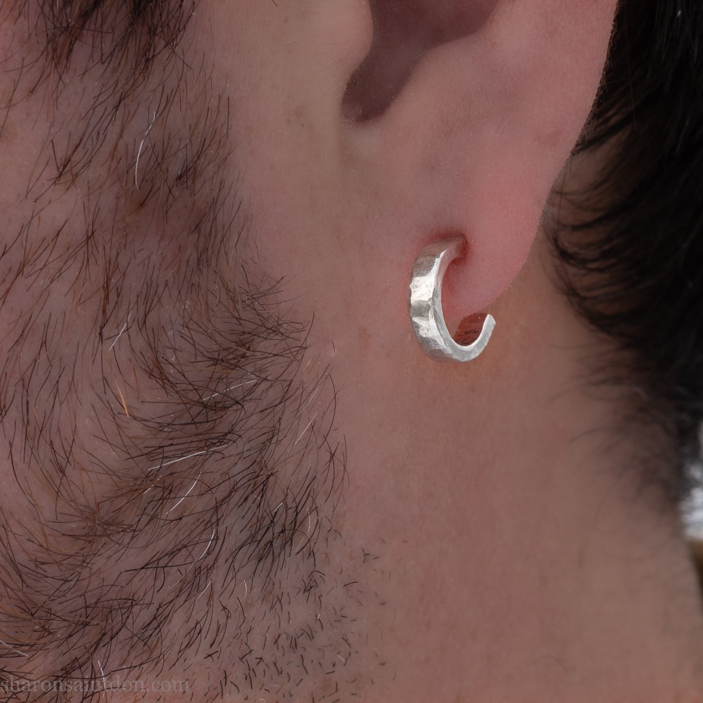 A close-up view of a person wearing handcrafted solid silver hoop earrings, 12mm diameter x 3mm wide x 1.5mm thick with a hammered matte finish.