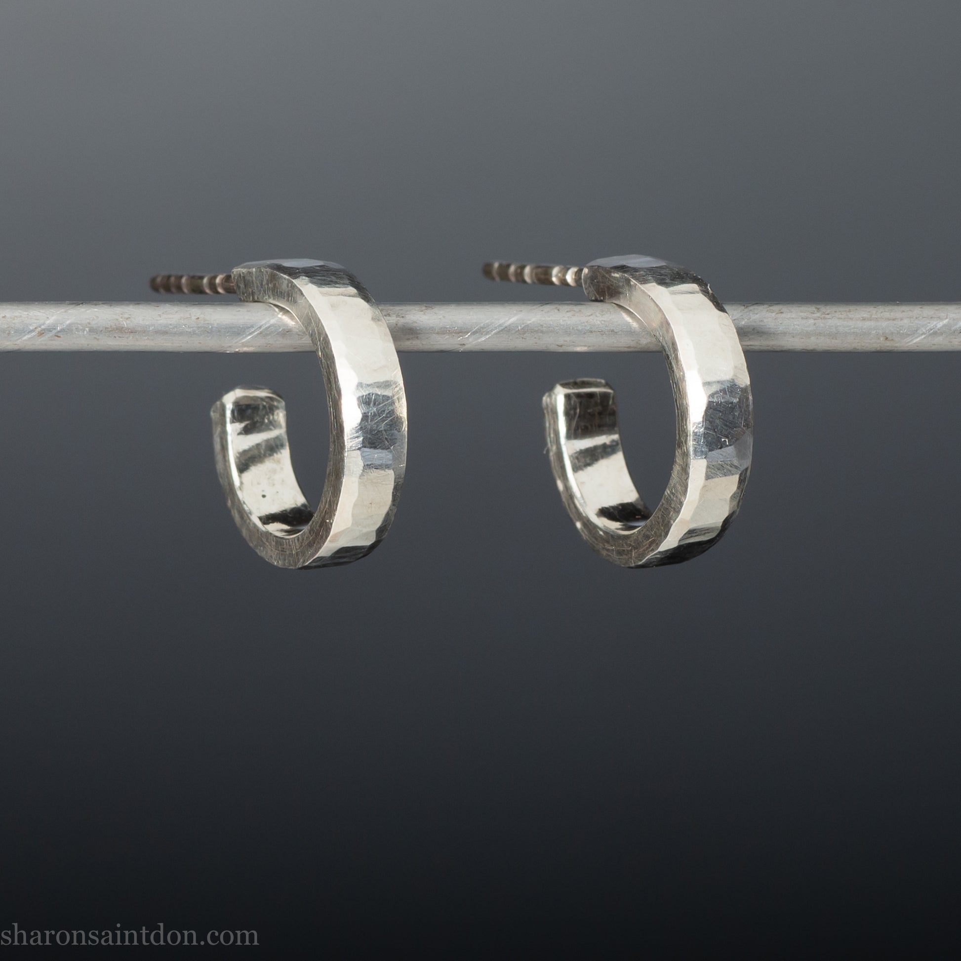 A close-up view of handcrafted solid silver hoop earrings, 14mm diameter x 3mm wide x 1.5mm thick with a hammered matte finish.