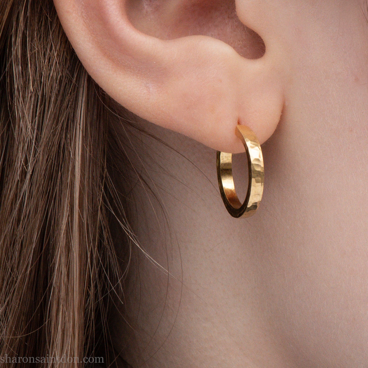 Solid gold hoop earrings worn on ear, handcrafted hammered finish. 16mm diameter, 2mm wide.