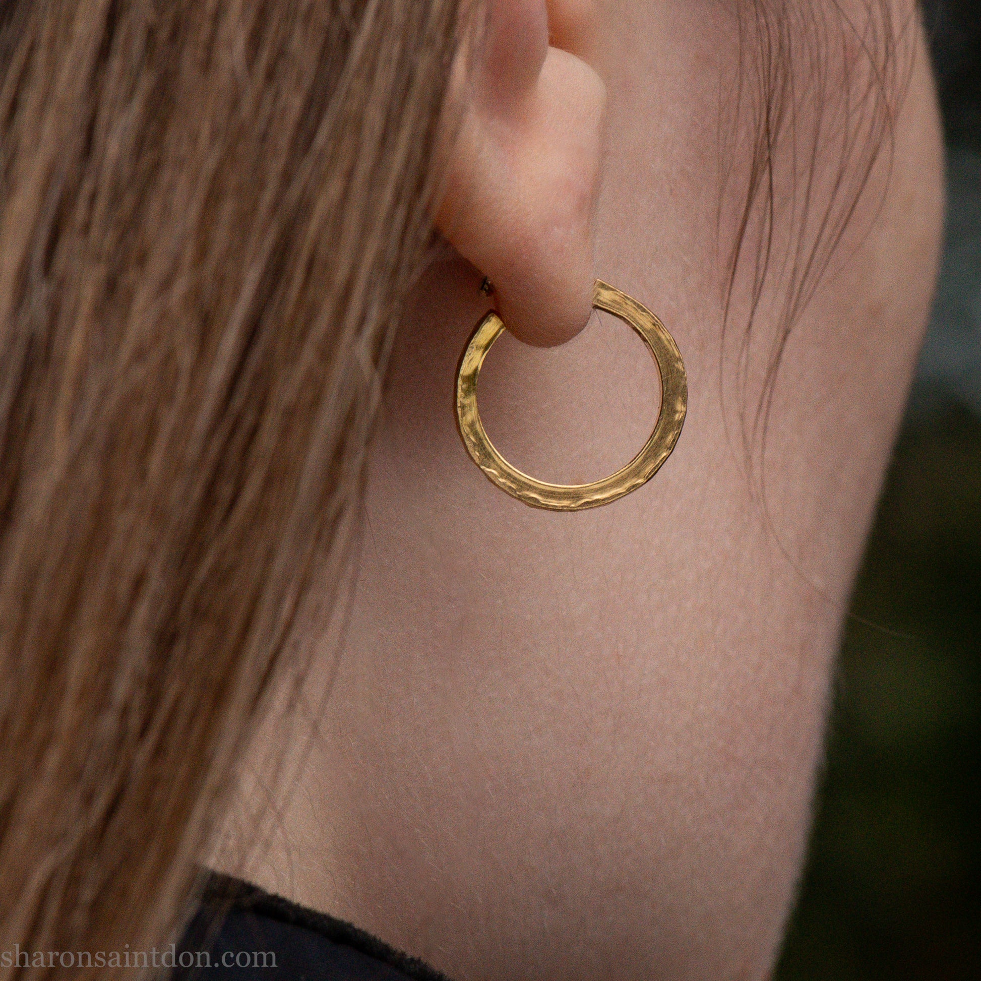 Solid gold hoop earrings worn on ear, handcrafted hammered finish. 16mm diameter, 2mm wide.