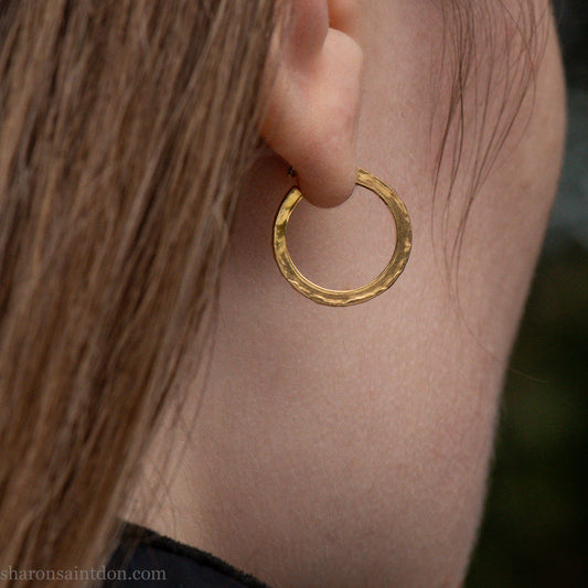 Solid gold hoop earrings worn on ear, handcrafted hammered finish. 16mm diameter, 2mm wide.