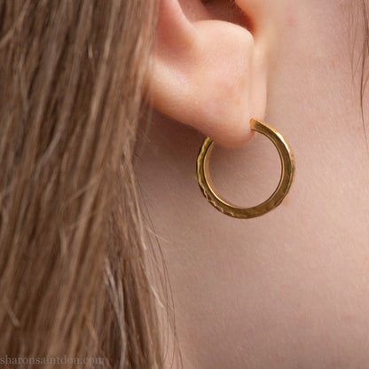 Solid gold hoop earrings worn on ear, handcrafted hammered finish. 16mm diameter, 2mm wide.