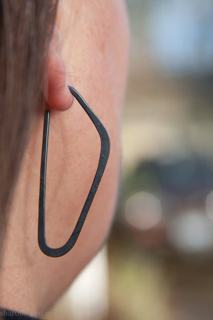 oxidized black sterling silver high D hoop earrings with hammered texture, 47mm long, shown on model’s ear.