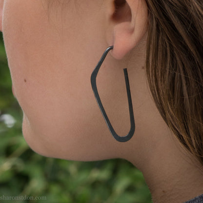 oxidized black sterling silver high D hoop earrings with hammered texture, 47mm long, shown on model’s ear