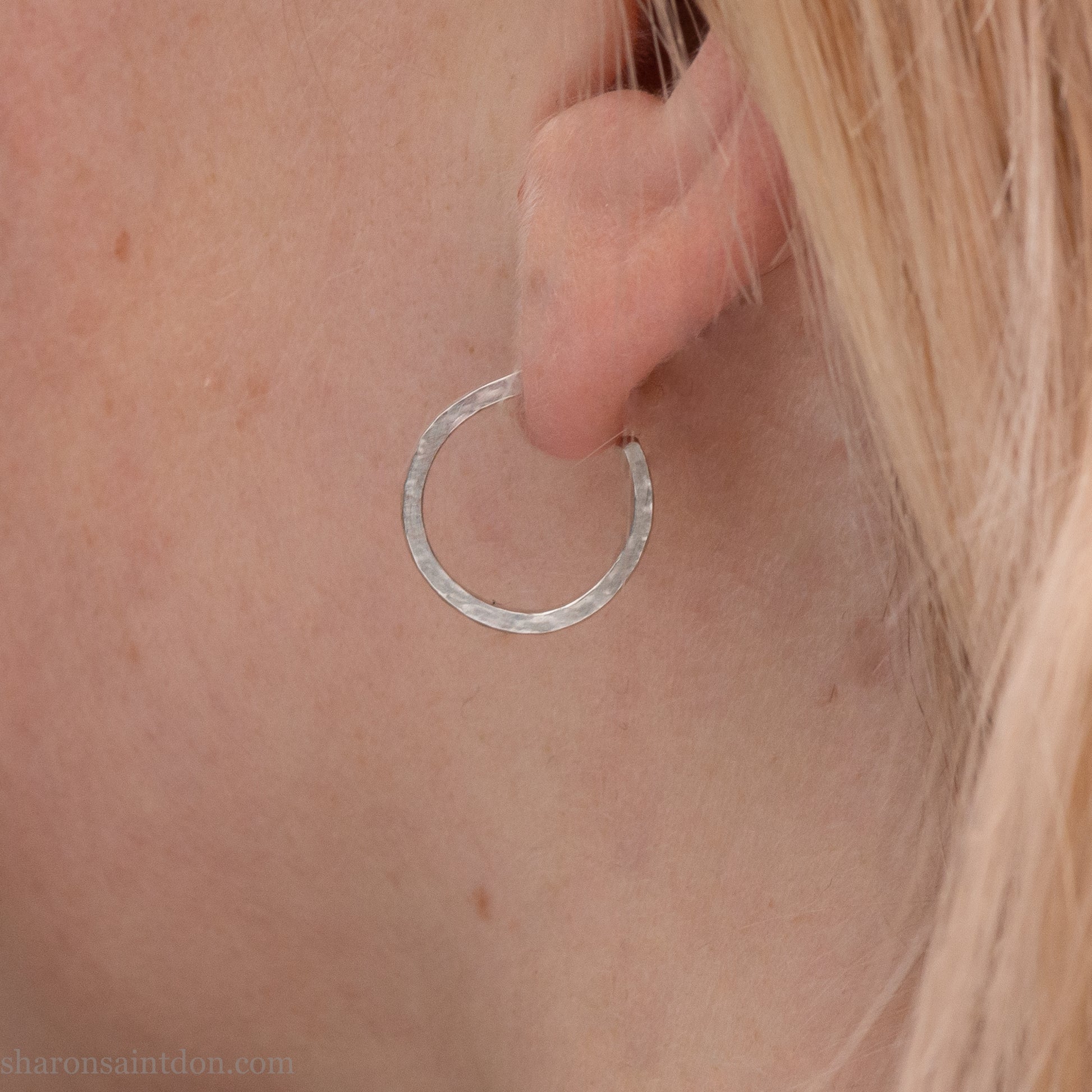 Close-up of a woman’s ear wearing a handcrafted 16mm sterling silver hoop earring with a matte hammered finish.