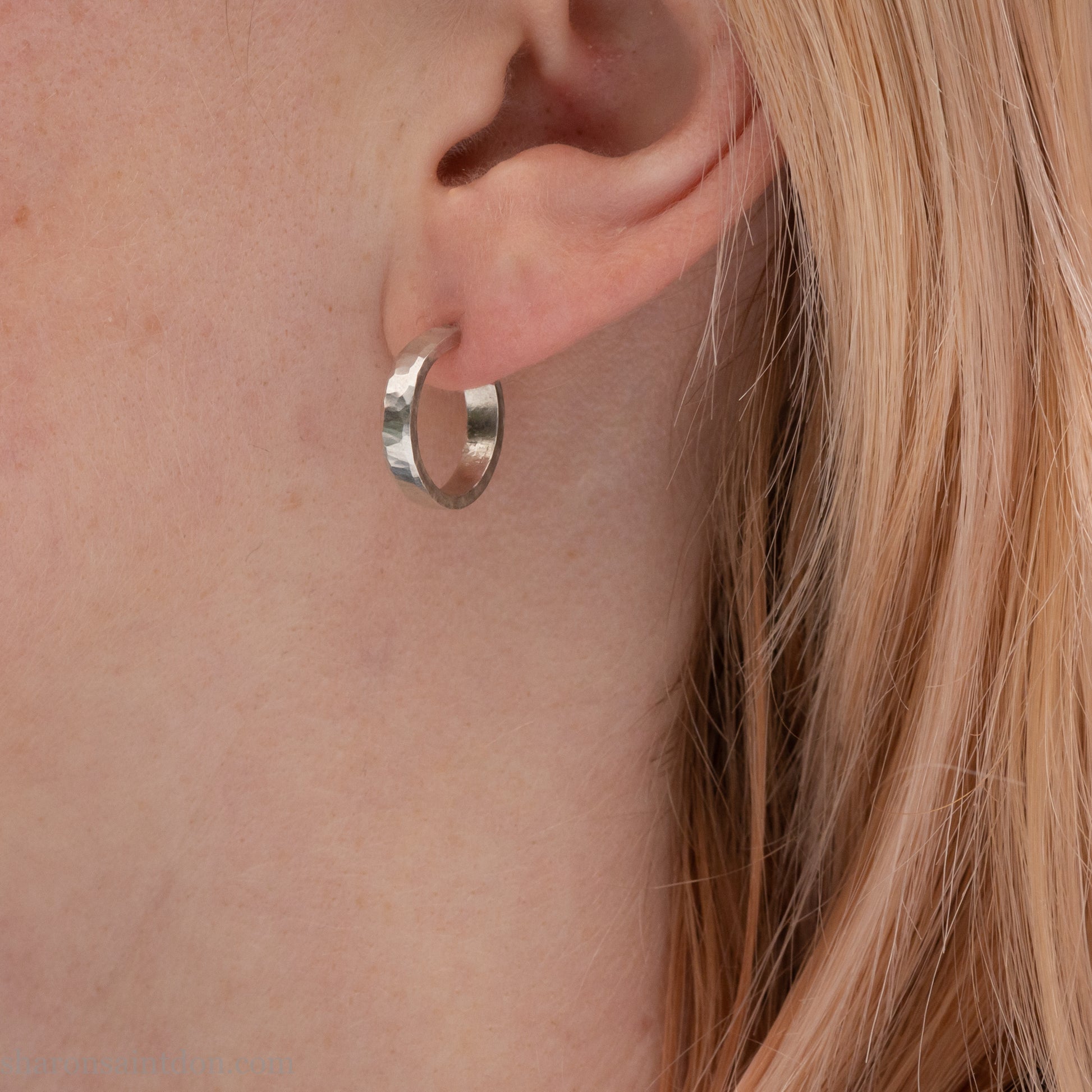 Close-up of a woman’s ear wearing a handcrafted 16mm sterling silver hoop earring with a matte hammered finish.
