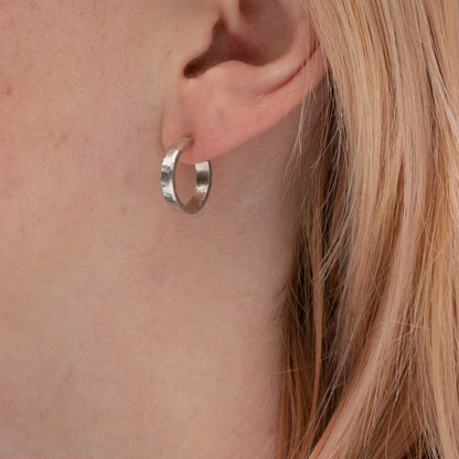 Close-up of a woman’s ear wearing a handcrafted 16mm sterling silver hoop earring with a matte hammered finish.