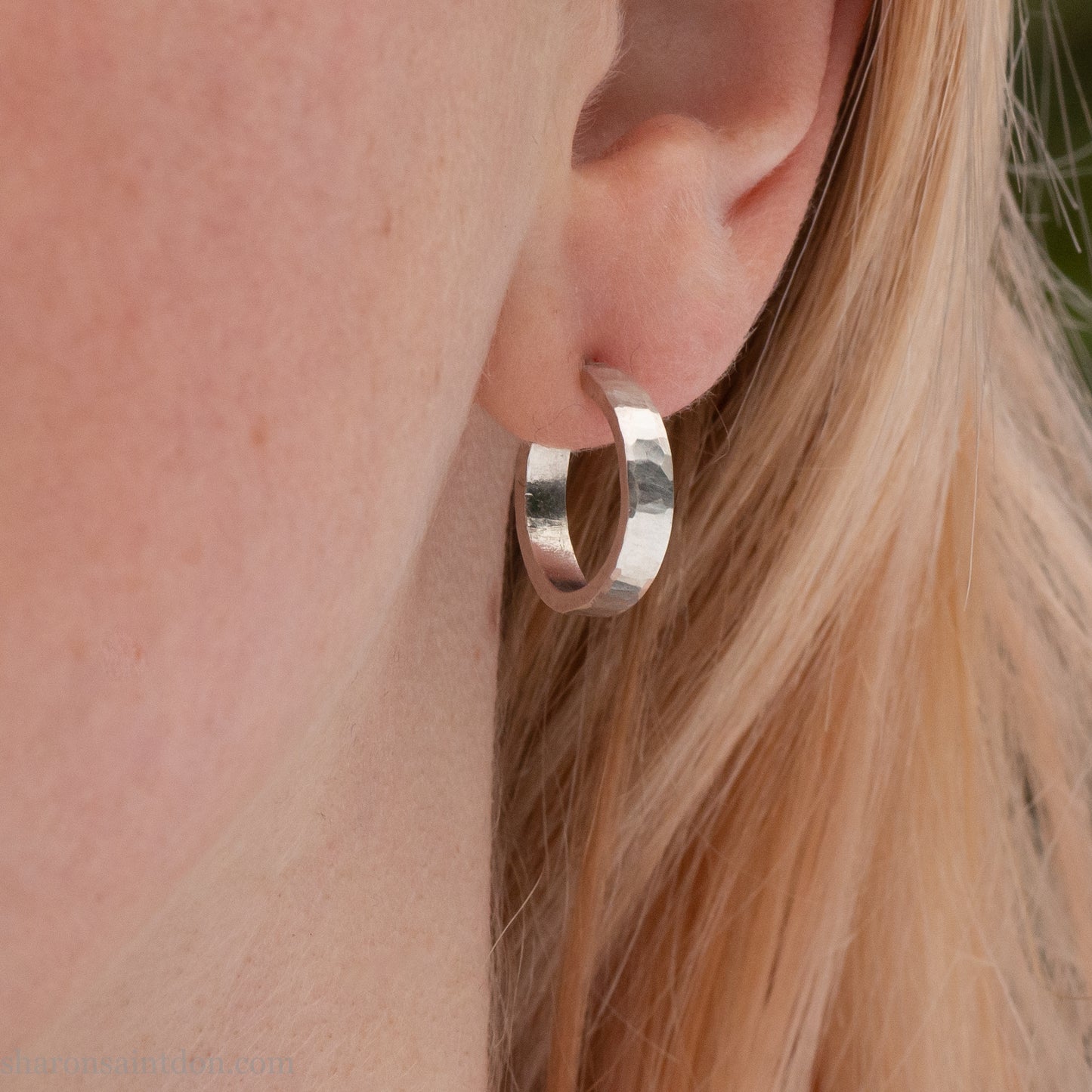 Close-up of a woman’s ear wearing a handcrafted 16mm sterling silver hoop earring with a matte hammered finish.