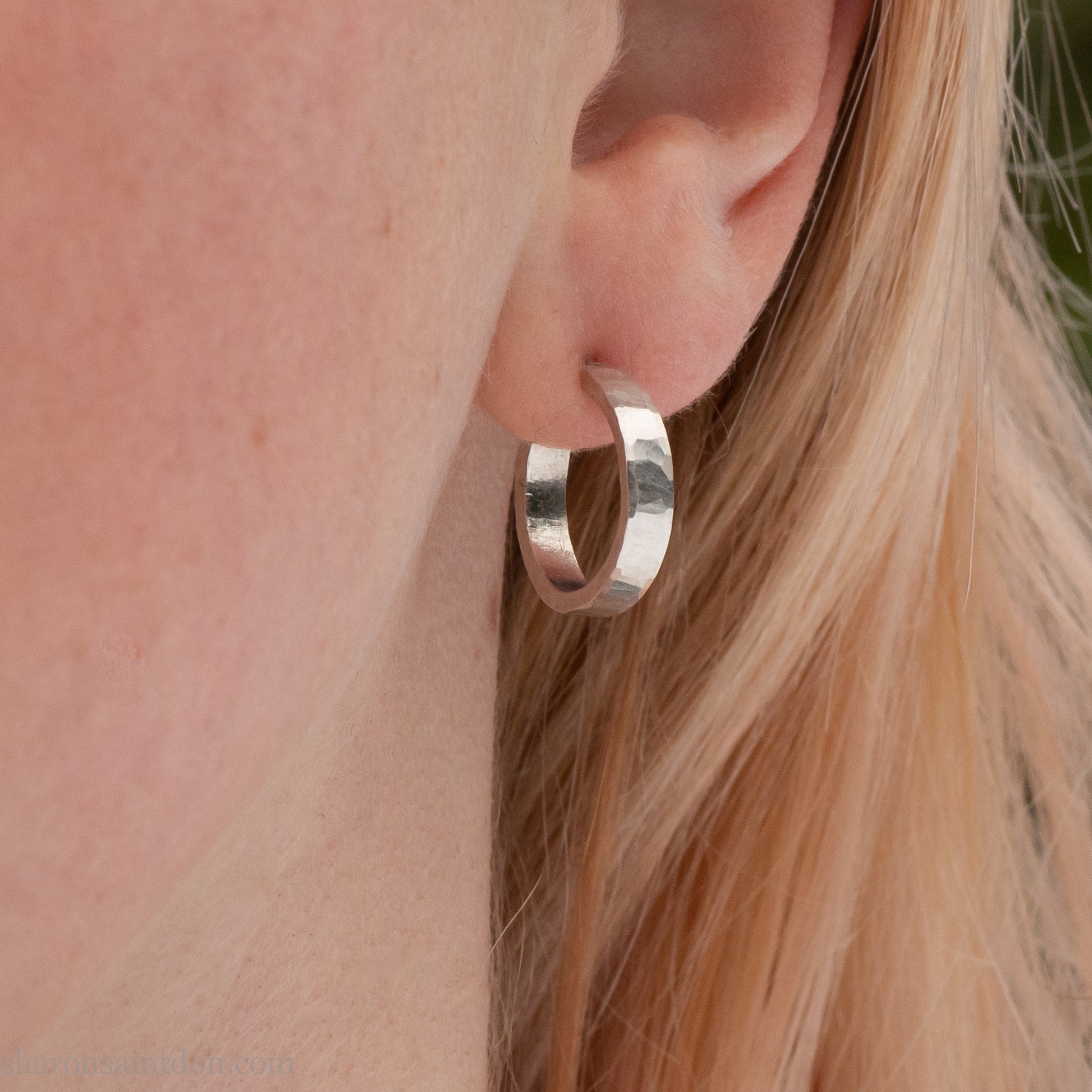 Close-up of a woman’s ear wearing a handcrafted 16mm sterling silver hoop earring with a matte hammered finish.