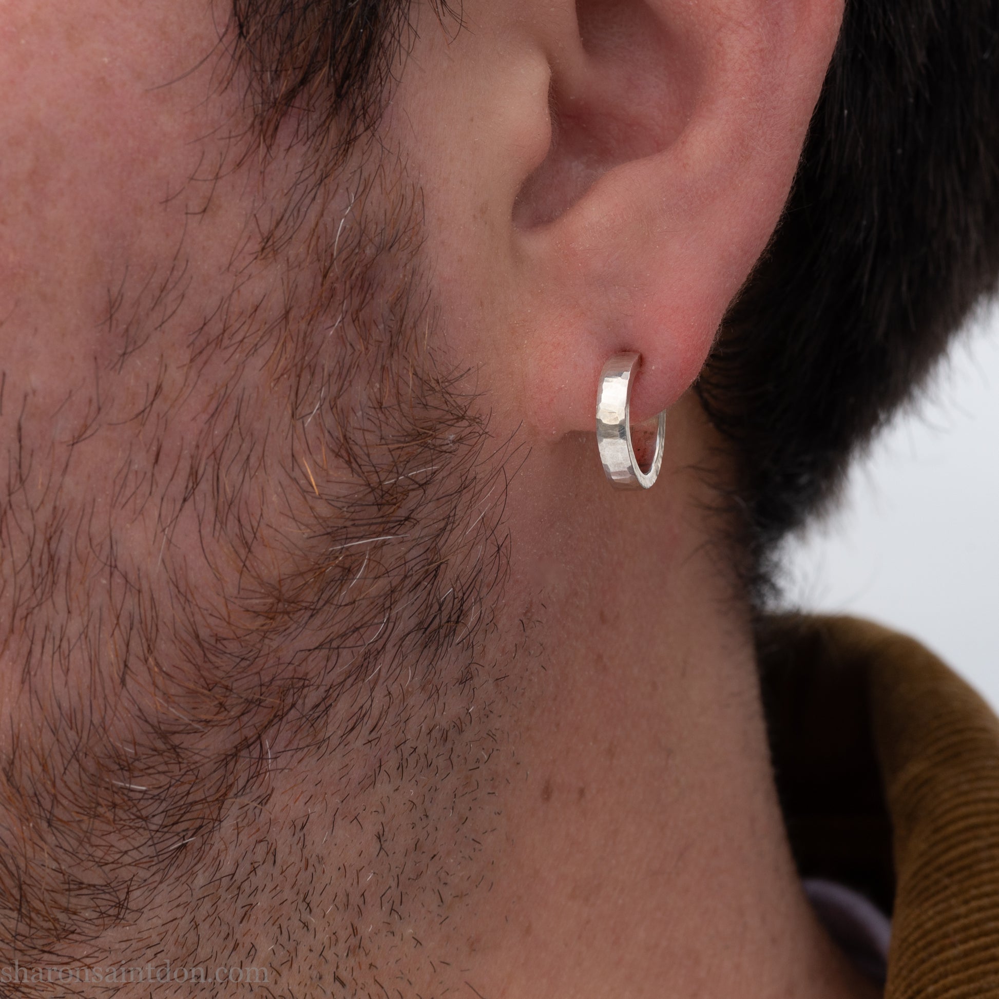 Close-up of a bearded man wearing a small handcrafted 16mm solid 925 sterling silver hoop earring with a matte hammered finish.