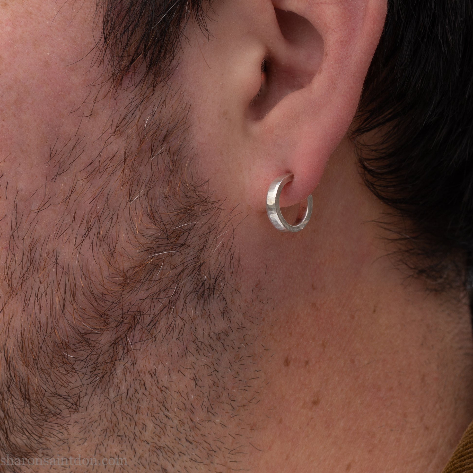 Close-up of a bearded man wearing a small handcrafted 16mm solid 925 sterling silver hoop earring with a matte hammered finish.