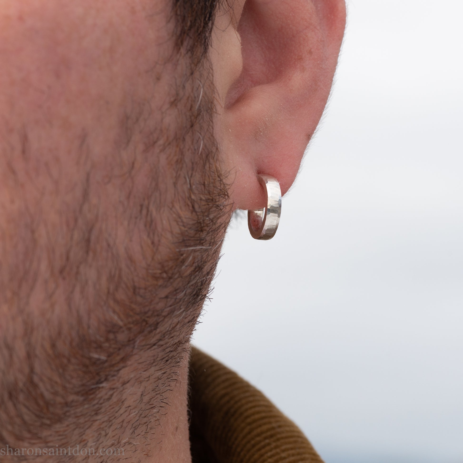 Close-up of a bearded man wearing a small handcrafted 16mm solid 925 sterling silver hoop earring with a matte hammered finish.