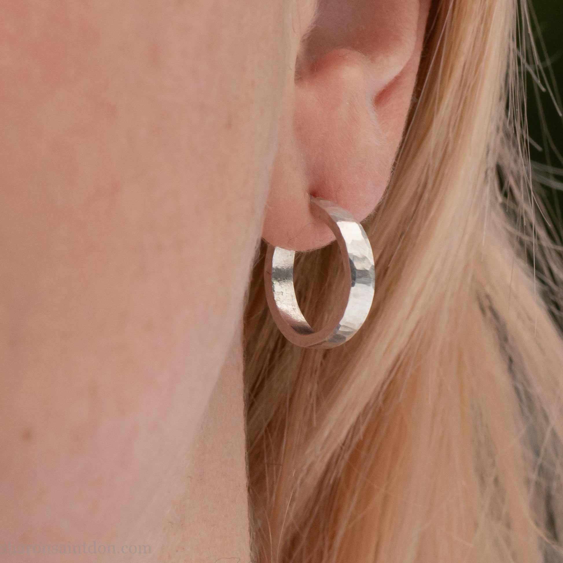 Close-up of a woman’s ear wearing a handcrafted 16mm sterling silver hoop earring with a matte hammered finish.