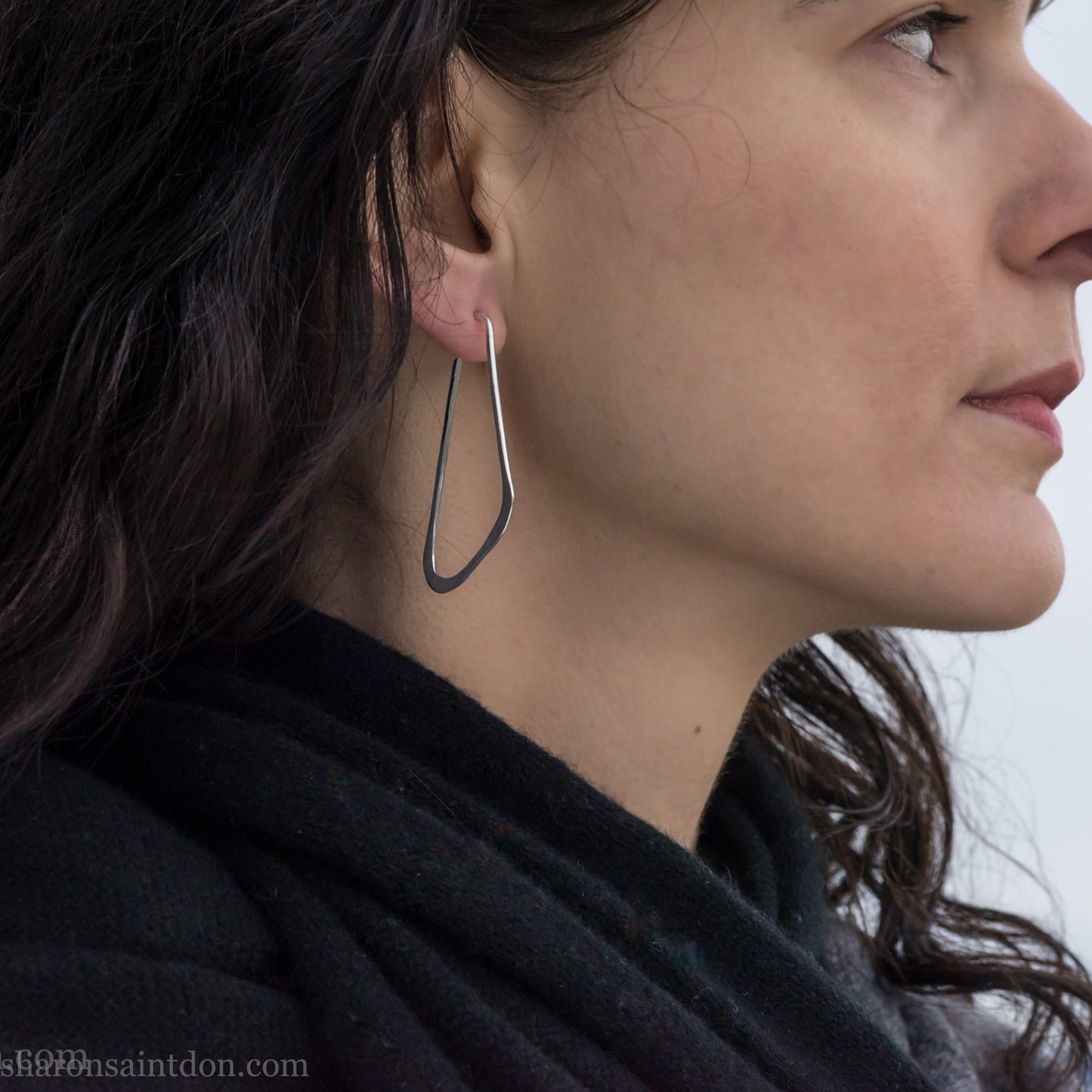 Woman wearing solid 925 sterling silver hoop earrings, angular low D shape, hand hammered.