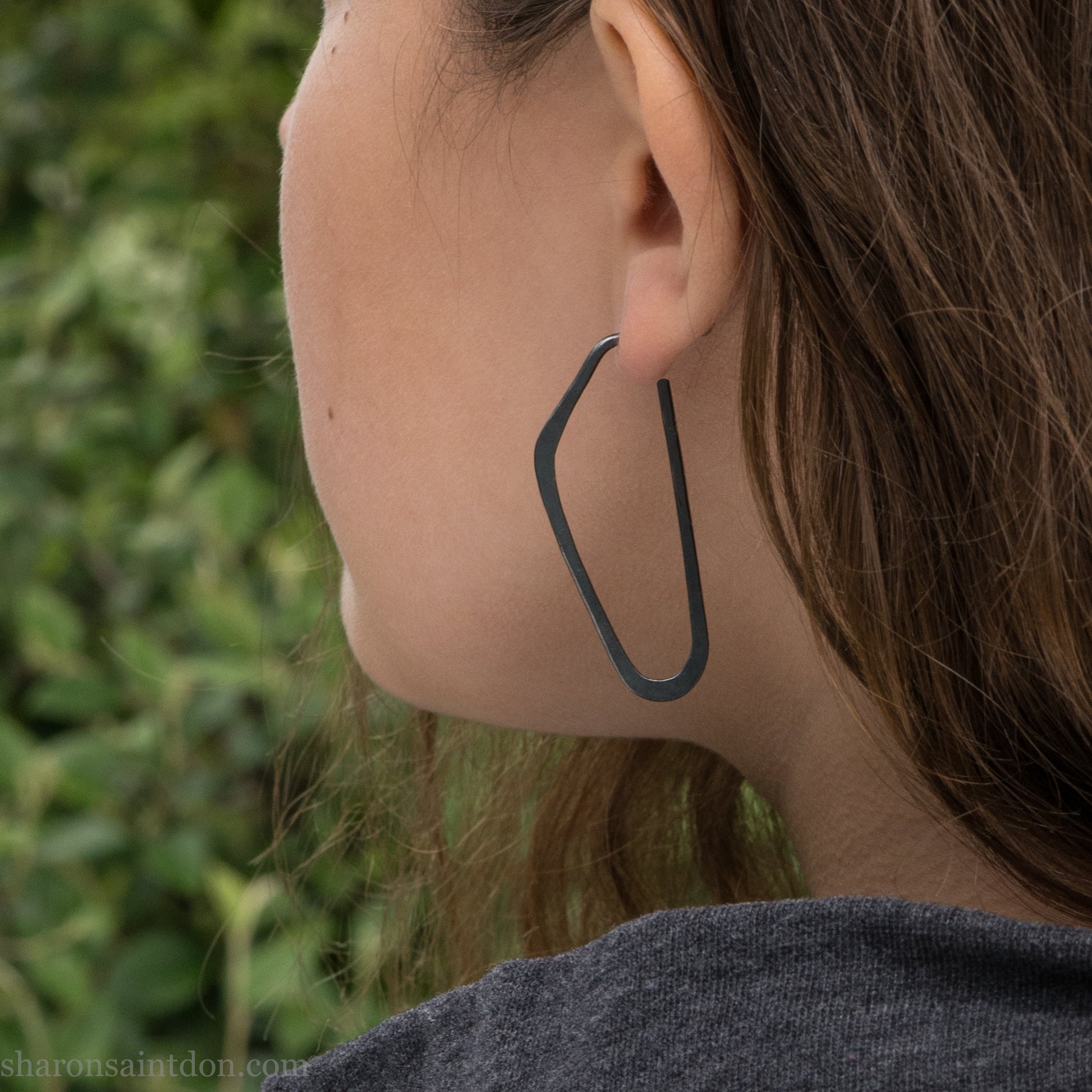 Person wearing hand hammered solid 925 sterling silver hoop earrings. Long, angular, high D shape, oxidized black, 47mm high x 19mm wide.