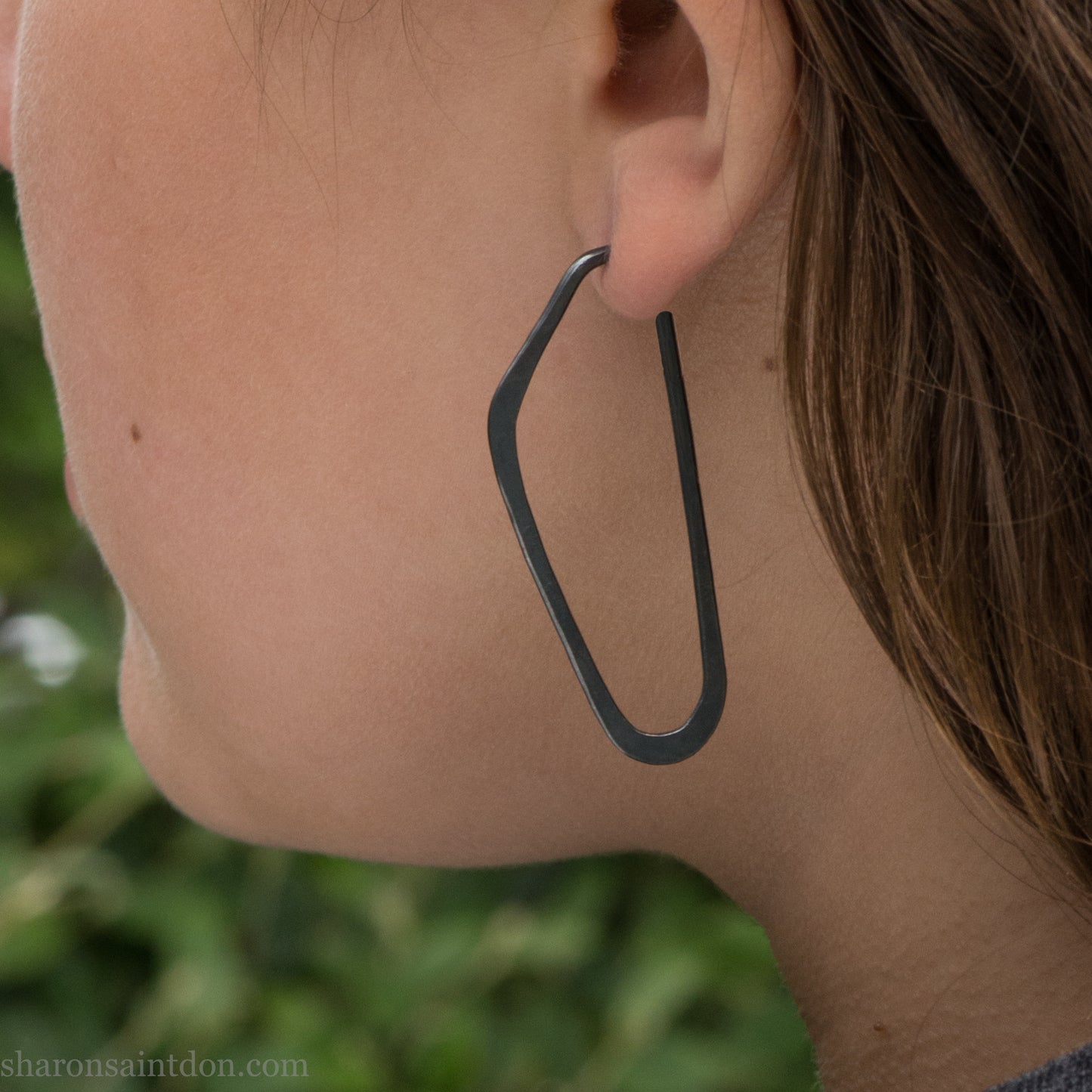 Person wearing hand hammered solid 925 sterling silver hoop earrings. Long, angular, high D shape, oxidized black, 47mm high x 19mm wide.