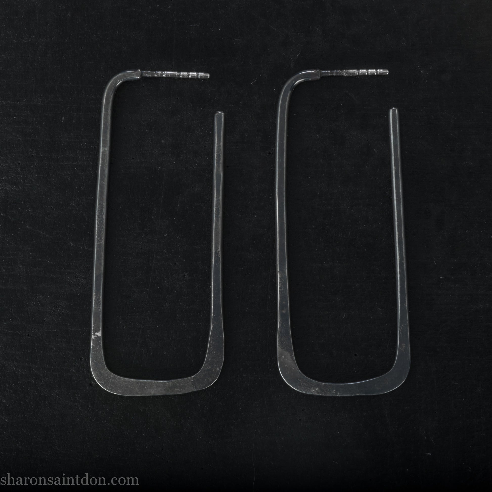 Person wearing hand hammered oxidized black rectangle hoop earrings in solid 925 sterling silver. 2x5cm, matte black patina.
