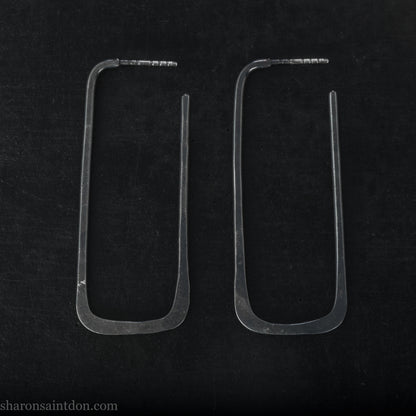Person wearing hand hammered oxidized black rectangle hoop earrings in solid 925 sterling silver. 2x5cm, matte black patina.