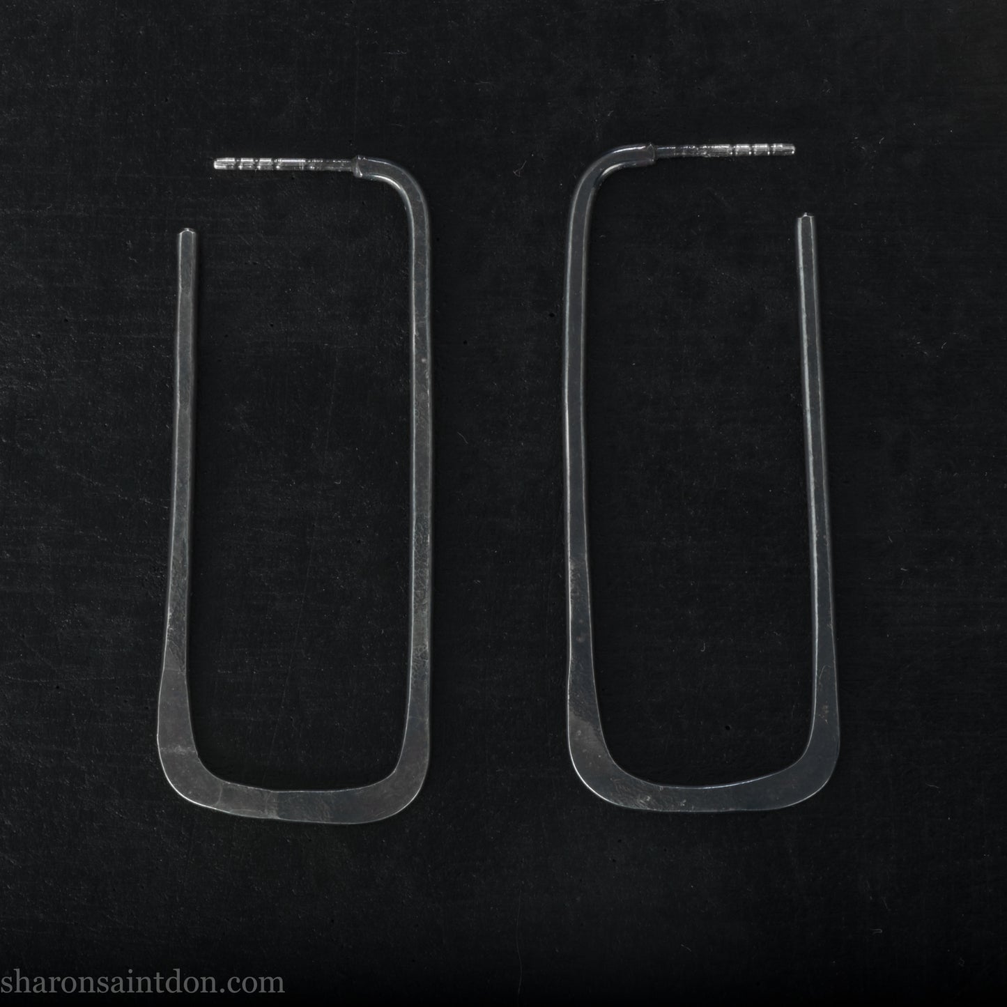 Person wearing hand hammered oxidized black rectangle hoop earrings in solid 925 sterling silver. 2x5cm, matte black patina.
