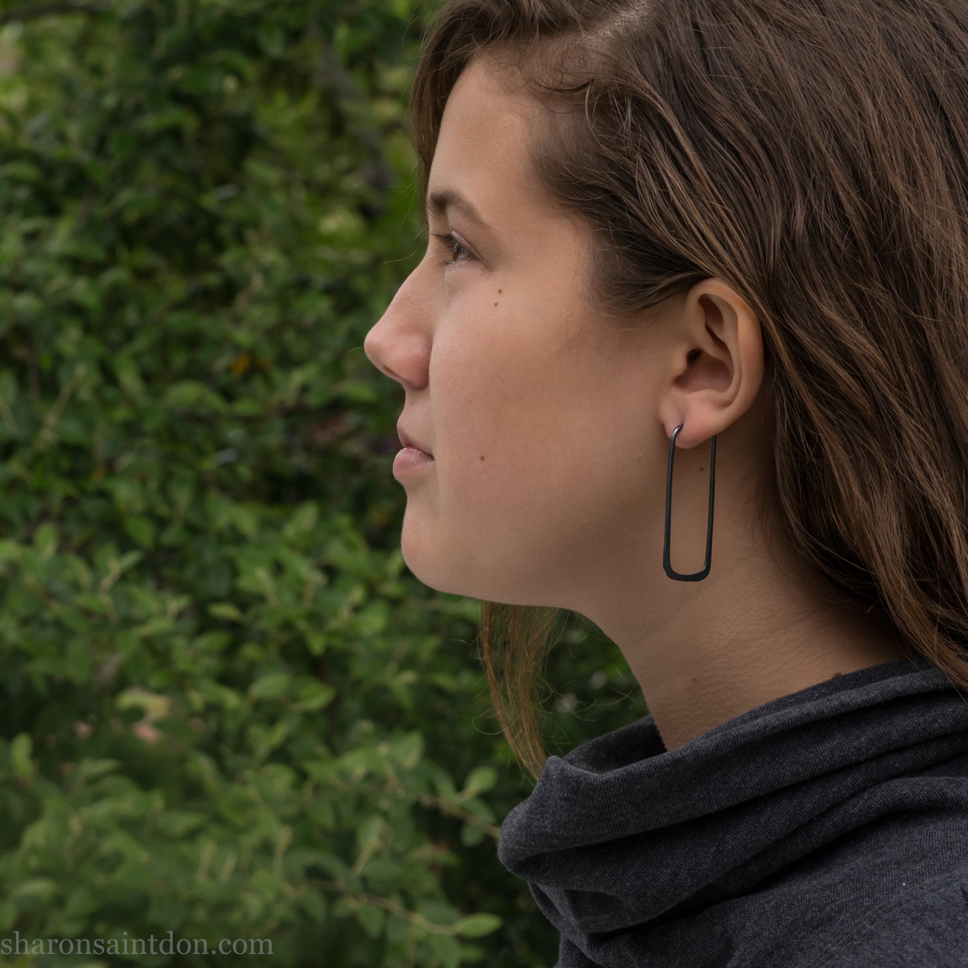 Person wearing hand hammered oxidized black rectangle hoop earrings in solid 925 sterling silver. 2x5cm, matte black patina.