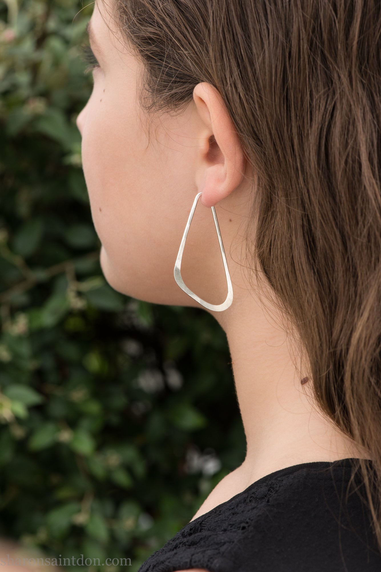 Woman wearing solid 925 sterling silver hoop earrings, angular low D shape, hand hammered.