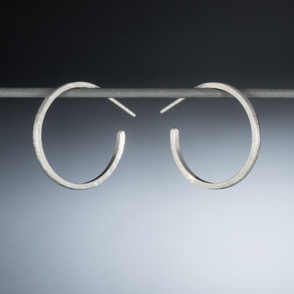 Hammered solid silver hoop earrings, handmade in the USA by Sharon Saint Don. 25mm diameter, 2mm wide, 1.5mm thick. solid silver posts and backs. Lightweight and comfortable for daily wear with a matte, brushed, shiny finish.