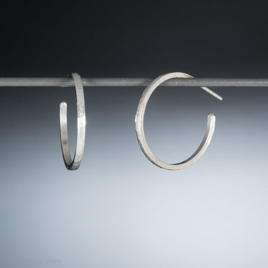 Hammered solid silver hoop earrings, handmade in the USA by Sharon Saint Don. 25mm diameter, 2mm wide, 1.5mm thick. solid silver posts and backs. Lightweight and comfortable for daily wear with a matte, brushed, shiny finish.