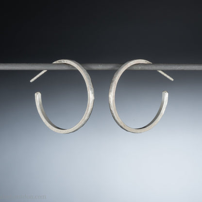 Hammered solid silver hoop earrings, handmade in the USA by Sharon Saint Don. 25mm diameter, 2mm wide, 1.5mm thick. solid silver posts and backs. Lightweight and comfortable for daily wear with a matte, brushed, shiny finish.