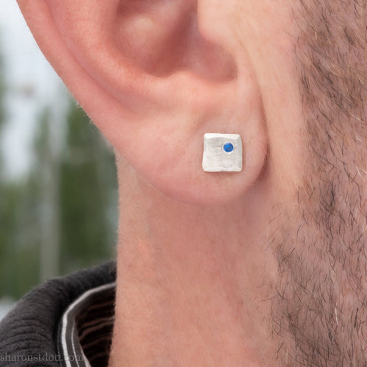 Handmade 925 sterling silver stud earrings  for men with 2mm, lab grown blue spinel gemstone set in the corner. 7mm square, 1.5mm thick with silver posts and backs and hammered, matte, brushed finish. Handmade by Sharon SaintDon in North America.