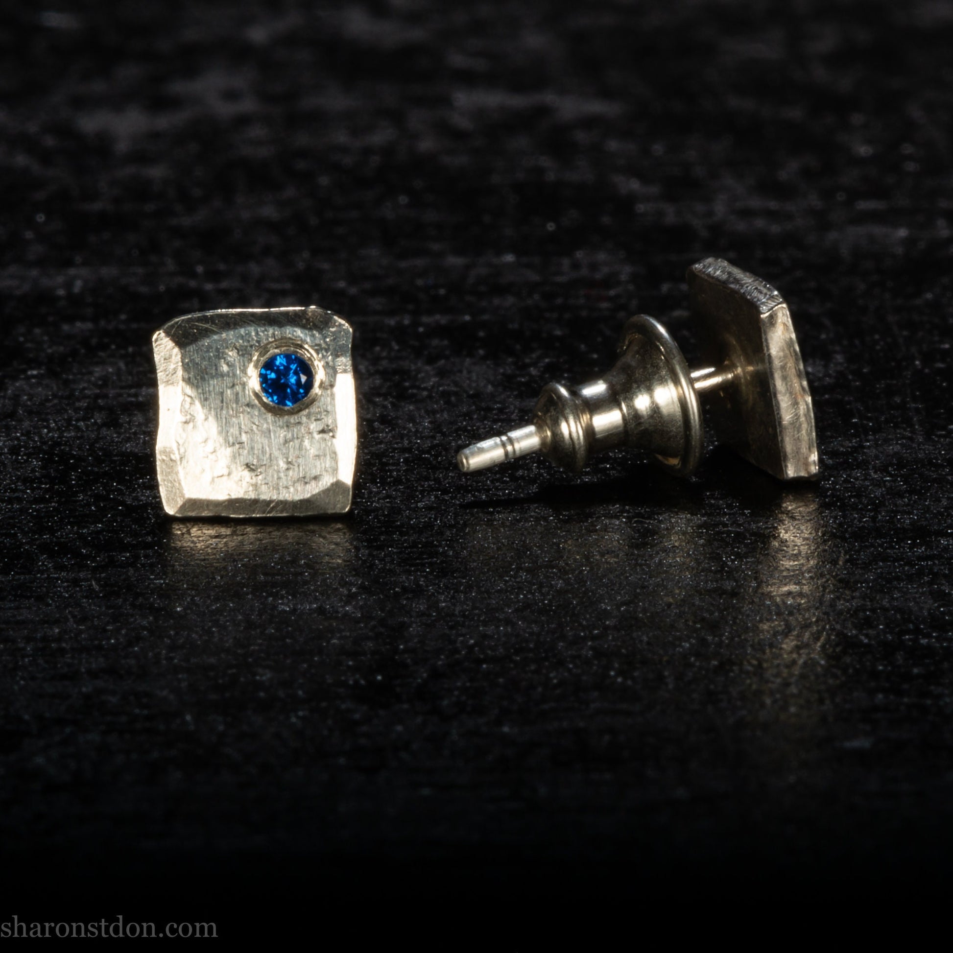 Handmade 925 sterling silver stud earrings  for men with 2mm, lab grown blue spinel gemstone set in the corner. 7mm square, 1.5mm thick with silver posts and backs and hammered, matte, brushed finish. Handmade by Sharon SaintDon in North America.