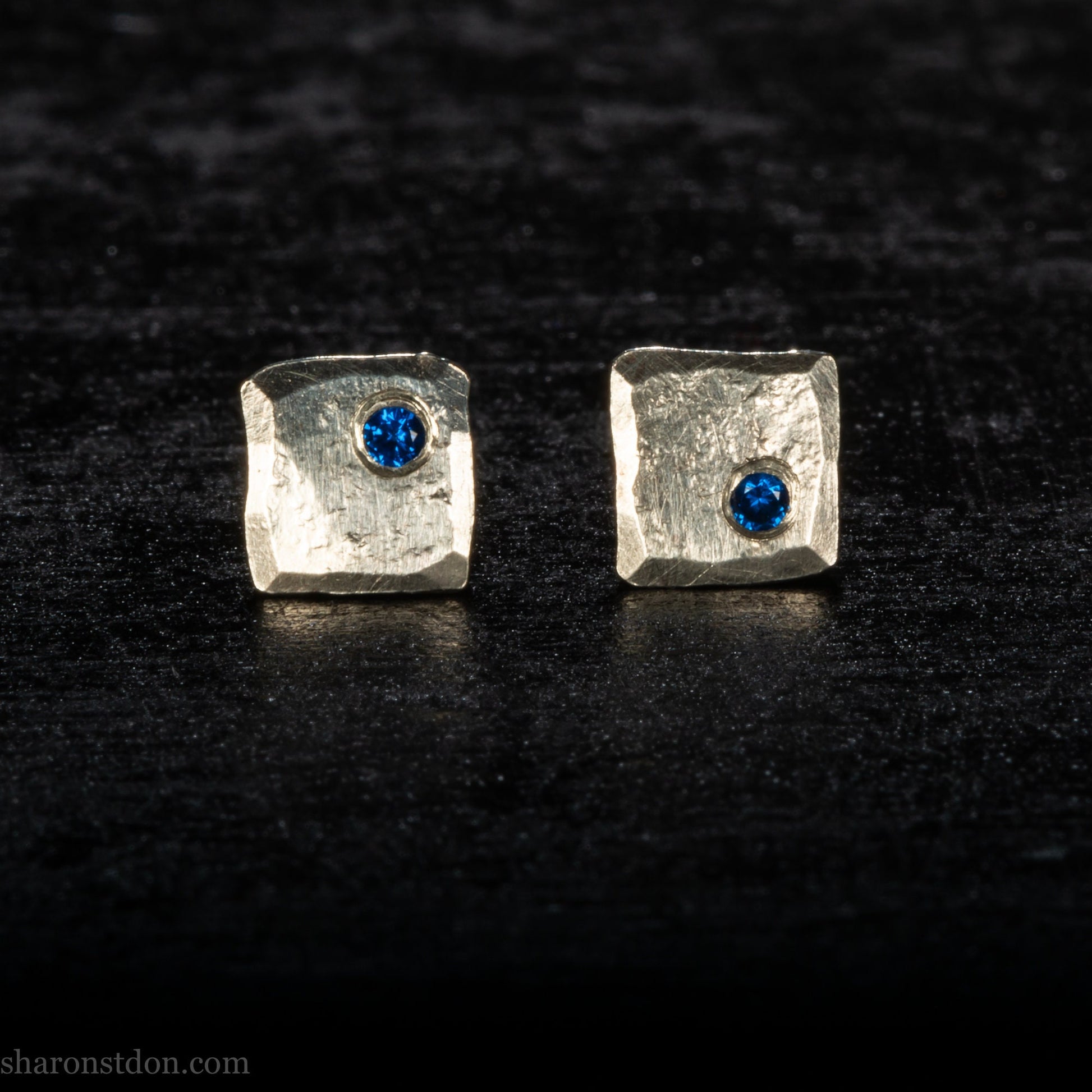 Handmade 925 sterling silver stud earrings  for men with 2mm, lab grown blue spinel gemstone set in the corner. 7mm square, 1.5mm thick with silver posts and backs and hammered, matte, brushed finish. Handmade by Sharon SaintDon in North America.