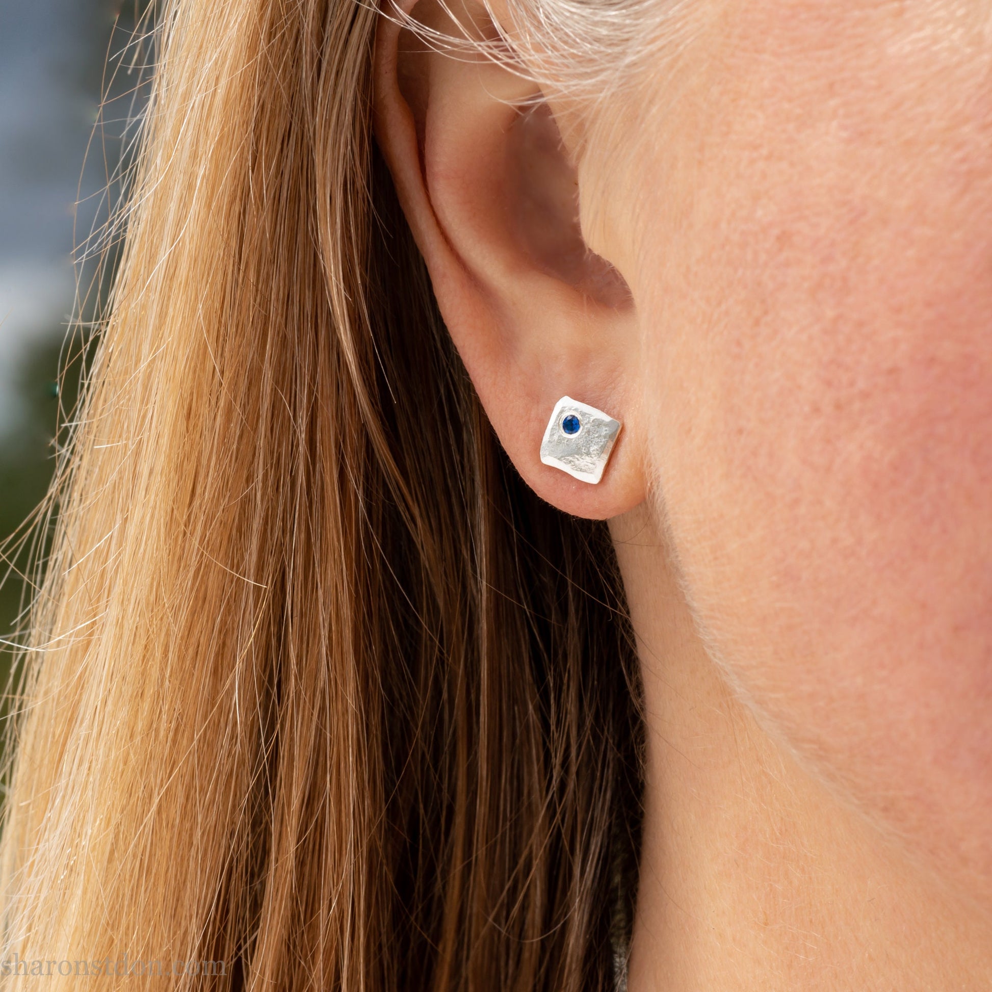 Handmade 925 sterling silver stud earrings  for men with 2mm, lab grown blue spinel gemstone set in the corner. 7mm square, 1.5mm thick with silver posts and backs and hammered, matte, brushed finish. Handmade by Sharon SaintDon in North America.