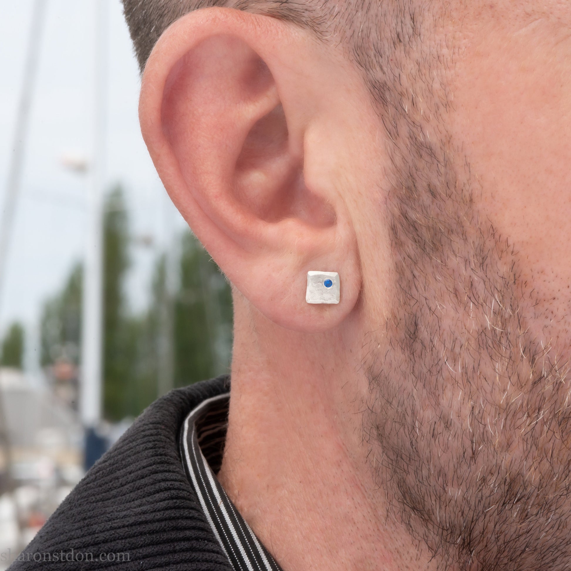 Handmade 925 sterling silver stud earrings  for men with 2mm, lab grown blue spinel gemstone set in the corner. 7mm square, 1.5mm thick with silver posts and backs and hammered, matte, brushed finish. Handmade by Sharon SaintDon in North America.