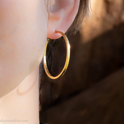 40mm diameter by 1.5mm thick handmade solid 18k yellow gold hoop earrings. Handmade by Sharon SaintDon in North America. Hammered from solid gold with a matte finish.