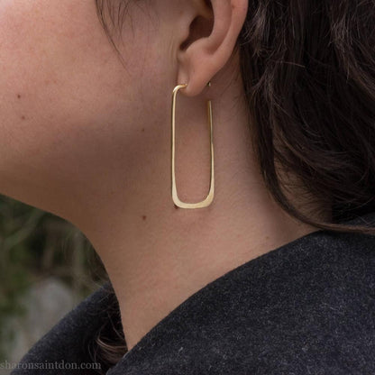 Large gold hoop earrings handmade by Sharon SaintDon in the Pacific Northwest of North America.  Hand forged solid 18k yellow gold rectangles, 2cm wide x 5cm long with a matte brushed finish. The locking backs and posts are also solid 18k gold.