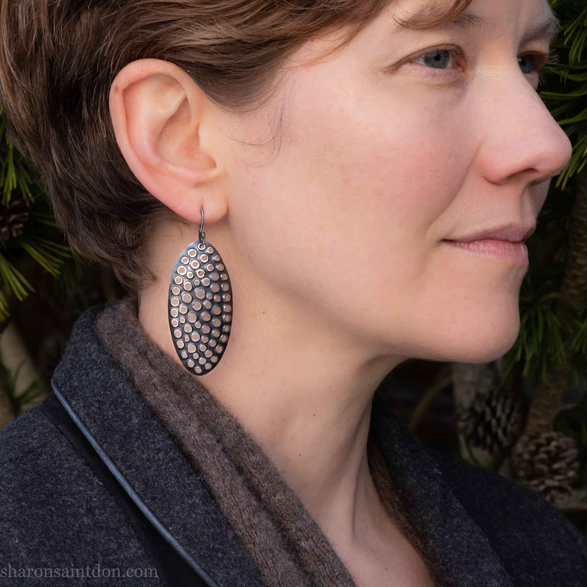 925 sterling silver dangle earrings, 50mm tall ovals with mesh holes punched by hand, and handmade ear wire french hooks. Oxidized black, dark patina rubbed back to shiny white shiny raised circles around the holes like little craters.