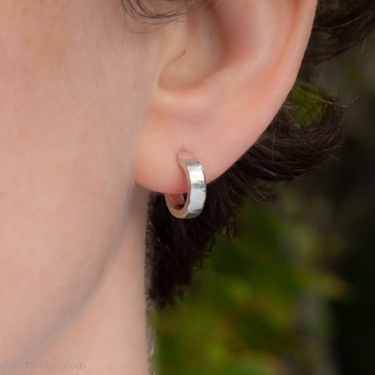 12mm diameter x 3mm wide x 2mm thick, small 925 sterling silver hoop earrings handmade by Sharon Saint Don in the USA. Solid hammered silver with a matte brushed finish, solid silver posts and backs.