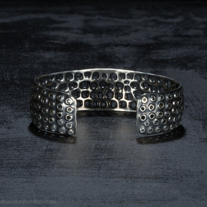925 sterling silver cuff bracelet handmade in USA. 2cm wide, 40cm x 60cm oval with approximately 28mm flexible opening for wrist. Punched perforated hole texture, oxidized black and rubbed back to show circles as white shiny silver.