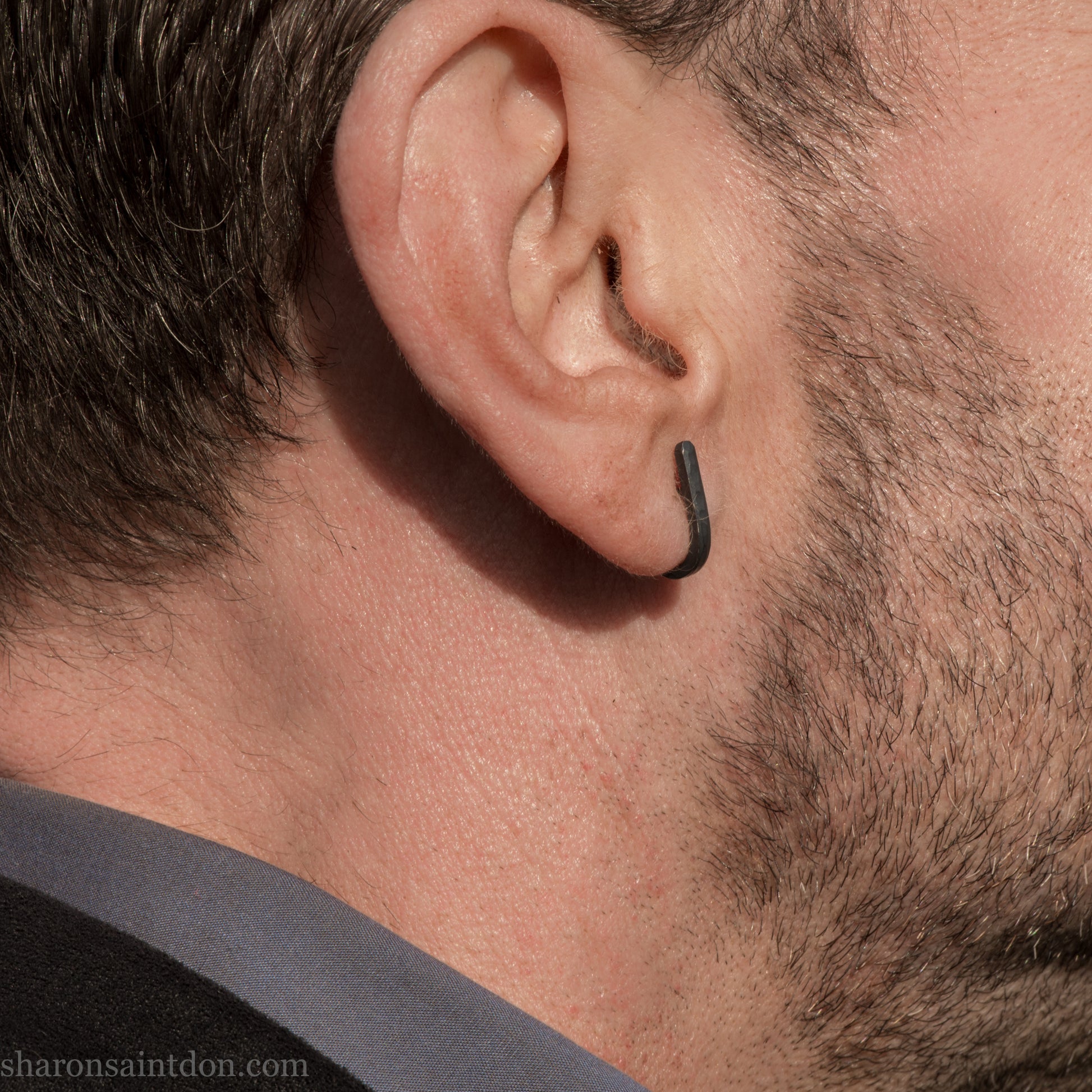 Hand hammered oxidized black sterling silver J-Curve hoop earrings, oxidized black patina, worn on ear.