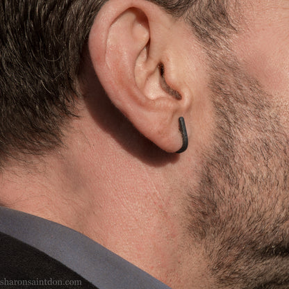 Hand hammered oxidized black sterling silver J-Curve hoop earrings, oxidized black patina, worn on ear.