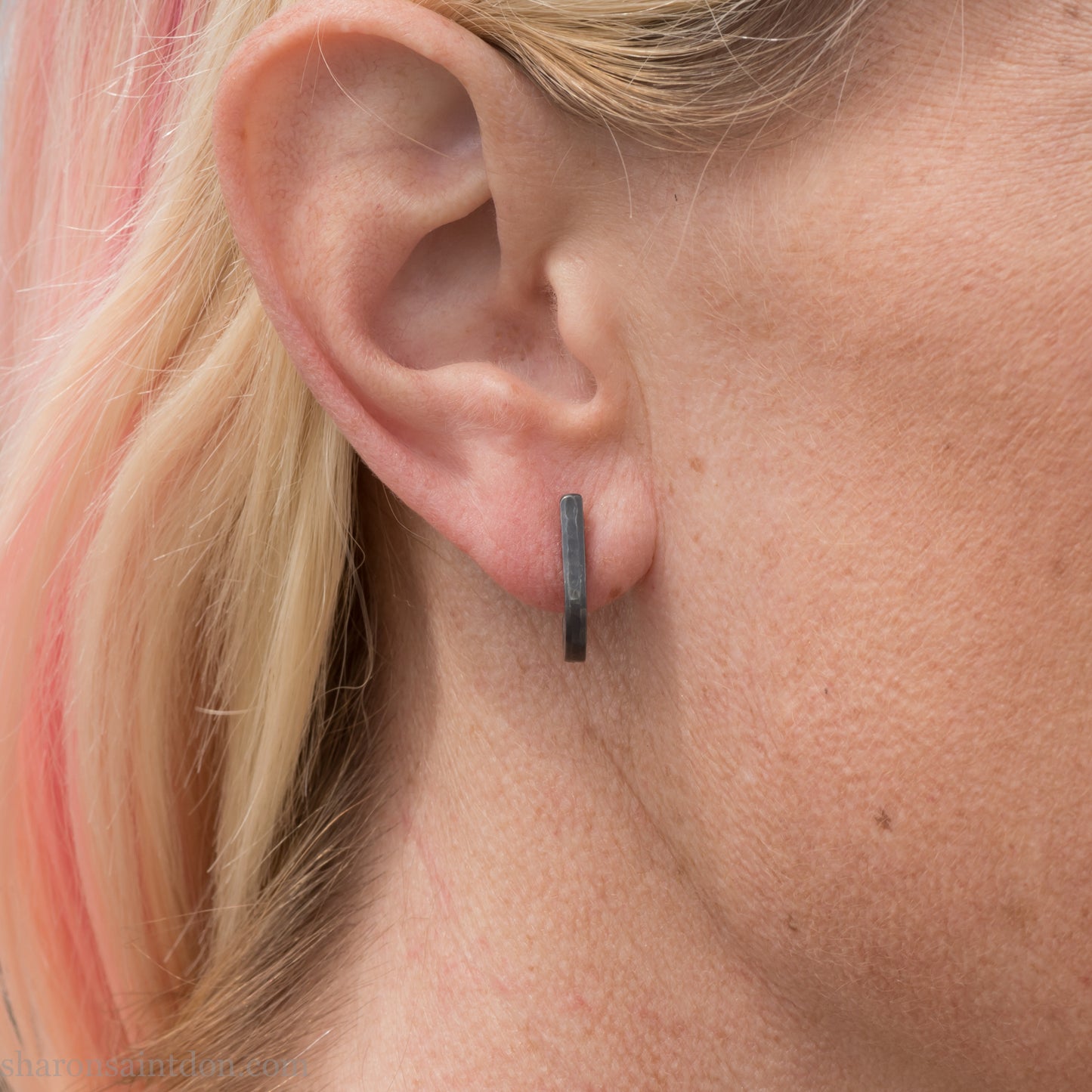 Hand hammered oxidized black sterling silver J-Curve hoop earrings, oxidized black patina, worn on ear.