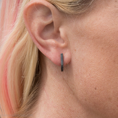 Hand hammered oxidized black sterling silver J-Curve hoop earrings, oxidized black patina, worn on ear.